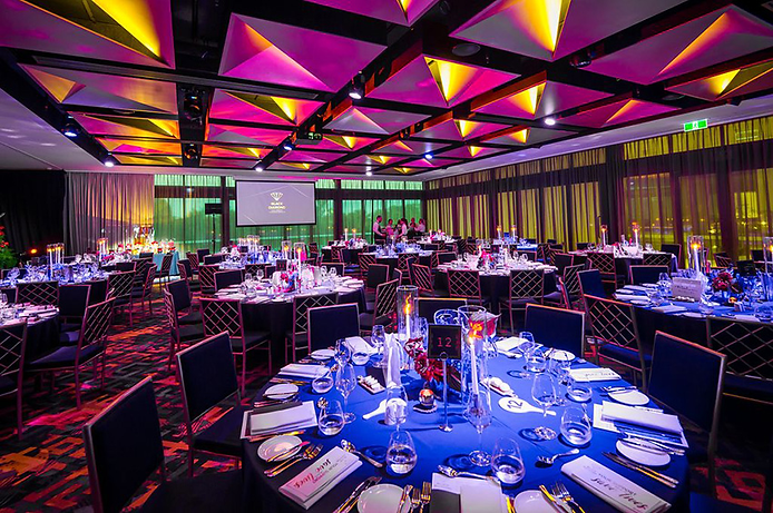 Elegant banquet hall at Beaumonde on the Point with colorful triangular ceiling lights, round tables set with blue tablecloths, glasses, and plates; vibrant ambiance.